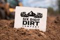 Six Digit Dirt Company sign in the dirt with construction equipment in the background